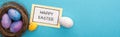 Top view of nest with Easter eggs near card with Happy Easter lettering on blue background, panoramic shot. Royalty Free Stock Photo
