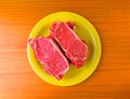 Top view of New York strip steaks on a bright yellow plate atop a wood countertop