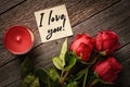 Top view note with the words I love you! and red roses with aroma candle on a wooden background: concept of assurance of love