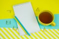 notebook with blank white paper sheet, pencilsand cup of tea on a blue and yellow trendy vibrant background