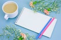 notebook with empty white paper sheet ,colored pencils,coffe with cream cup and floral frame on a pastel blue background Royalty Free Stock Photo