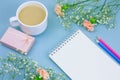 notebook with empty white paper sheet ,colored pencils,coffe with cream cup and floral frame on a pastel blue background Royalty Free Stock Photo