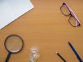 Top view of notebook, light bulb, pink glasses, Magnifying glass pen and pencil on wooden table with center copy space