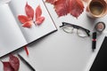 Top view of notebook near glasses, coffee cup, cosmetics, pen and red leaves of wild grapes on white table. Royalty Free Stock Photo