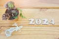 Top view of the number 2024 carved in wood, flowerpot with succulent and cactus, and miniature bicycle on wooden table. Concept of