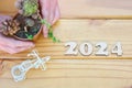 Top view of the number 2024 carved in wood, hands holding flowerpot with succulent and cactus, and miniature bicycle on wooden