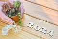 Top view of the number 2024 carved in wood, hands holding flowerpot with succulent and cactus, and miniature bicycle on wooden