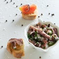 Top view of octopus salad with slices of toasted baguette - bruschetta on white background with black pepper and sea salt.