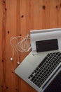 Top view of an office mock up with a laptop, blank mobile phone with headsets, and blank notebook