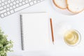 Top view of office table. On desk have notebook, Teacup, Bread, Laptop, and pencil on white ground