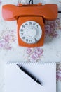Top view of an old analog orange phone and pen and notebook Royalty Free Stock Photo