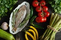 Top view of fresh raw dorada fish in a white dish with a set of vegetables on a black table Royalty Free Stock Photo