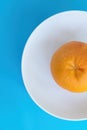 Top view of one orange grapefruit on white plate on blue background. Diet concept, vertical view Royalty Free Stock Photo