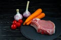 Top view of one pieces raw pork chop steaks with cherry tomatoes carrot and garlic on a black stone cutting board Royalty Free Stock Photo
