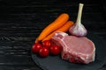 Top view of one pieces raw pork chop steaks with cherry tomatoes carrot and garlic on a black stone cutting board Royalty Free Stock Photo