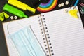 Top view of open notebook with face mask, colorful pencils, rainbow eraser, notebook, sticky notes. Flat lay. Royalty Free Stock Photo