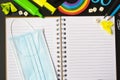 Top view of open notebook with face mask, colorful pencils, rainbow eraser, notebook, sticky notes. Flat lay Royalty Free Stock Photo