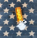 Top view of open prescription bottle filled with opioid pain killer tablets with USA rustic flag in background