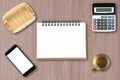 Top view of open spiral blank notebook with smartphone, calculator, empty bamboo basket, and cup of tea on wooden desk background Royalty Free Stock Photo