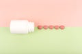 Top view of an opened white medication bottle with spilled red round pills on green and pink background with copy space Royalty Free Stock Photo