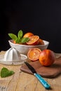 Top view of orange sanginas in bowl with white juicer, mint and blue knife on rustic wooden table and black background Royalty Free Stock Photo