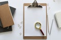 Top view over the working desk with notebooks, paper clips and white paper with magnificent glass on it. Copy space for text. Flat