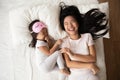 Happy Asian mom and little daughter relax in cozy bedroom