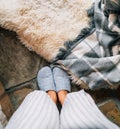 Top view of a pair of gray home slippers on female`s feet near the natural white sheep sheepskin with warm plaid dropped on the