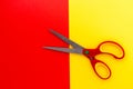 Top view of pair plastic open scissors with stainless steel blade on red-yellow background. Tool for cutting various thin