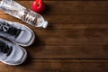 Top view of pair sports shoes, bottle water and red apple on wood table, Gray sneakers and accessories equipment in fitness GYM