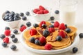 Top view of pancakes with caramel on plate with blueberries and raspberries with bowls, glass of milk and jug on white table, Royalty Free Stock Photo