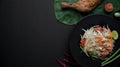 Top view of papaya salad on black plate, chicken grill on green taro a