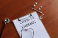 Top view of paper clipboard with text COVID-19 ENDEMIC, stethoscope, glass vial and syringe