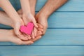 Top view of parents and kid holding pink heart in hands at turquoise wooden table, space for text. Family day Royalty Free Stock Photo