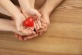 Top view of parents and kid holding red heart in hands at wooden table, space for text. Family day