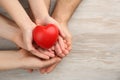 Top view of parents and kid holding red heart in hands at wooden table, space for text. Family day