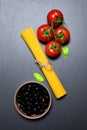 Top view: pasta or italian spaghetti, tomatoes, olives and oregano on black stone slate background Royalty Free Stock Photo