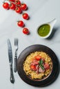 top view of pasta with mint leaves, jamon and cherry tomatoes covered by parmesan on plate at marble table with pesto in bowl, Royalty Free Stock Photo