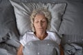 Top view of peaceful sleepy mature lady lying in bedding