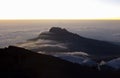 Top view of the peak of the mountain with clouds creeping over it against the background of the sunset Royalty Free Stock Photo
