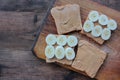 Top view of Peanut butter banana toasts on wooden background. Slices of whole wheat bran bread with peanut paste on cutting board Royalty Free Stock Photo