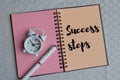 Top view of pen, clock and notebook written with text SUCCESS STEPS Royalty Free Stock Photo