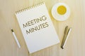 Top view of pen,a cup of coffee,and notebook written with Meeting Minutes on wooden background