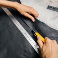 Top view of a person`s hands using cutting tool and metal ruler while producing leather goods