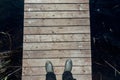 Top view of a person wearing green rubber boots standing on a wooden deck on water