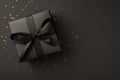 Top view photo of black giftbox with black ribbon bow and golden confetti on isolated black background with copyspace Royalty Free Stock Photo