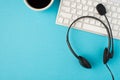 Top view photo of black headphones with microphone on white keyboard and cup of coffee on isolated light blue background with Royalty Free Stock Photo