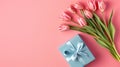 Top view photo of blue giftbox with ribbon bow and bouquet of pink tulips on isolated pastel pink background. Royalty Free Stock Photo