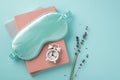 Top view photo of blue silk sleeping mask small white alarm clock on planners and sprig of lavender on isolated pastel blue
