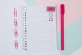 Top view photo of bright, positive stationery. Set of open, empty spiral notepad, paper clips and pen on blue and pink background Royalty Free Stock Photo